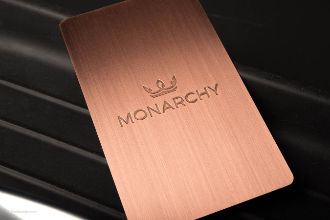 Premium copper metal business card with etched Monarchy logo on brushed finish, luxury branding.
