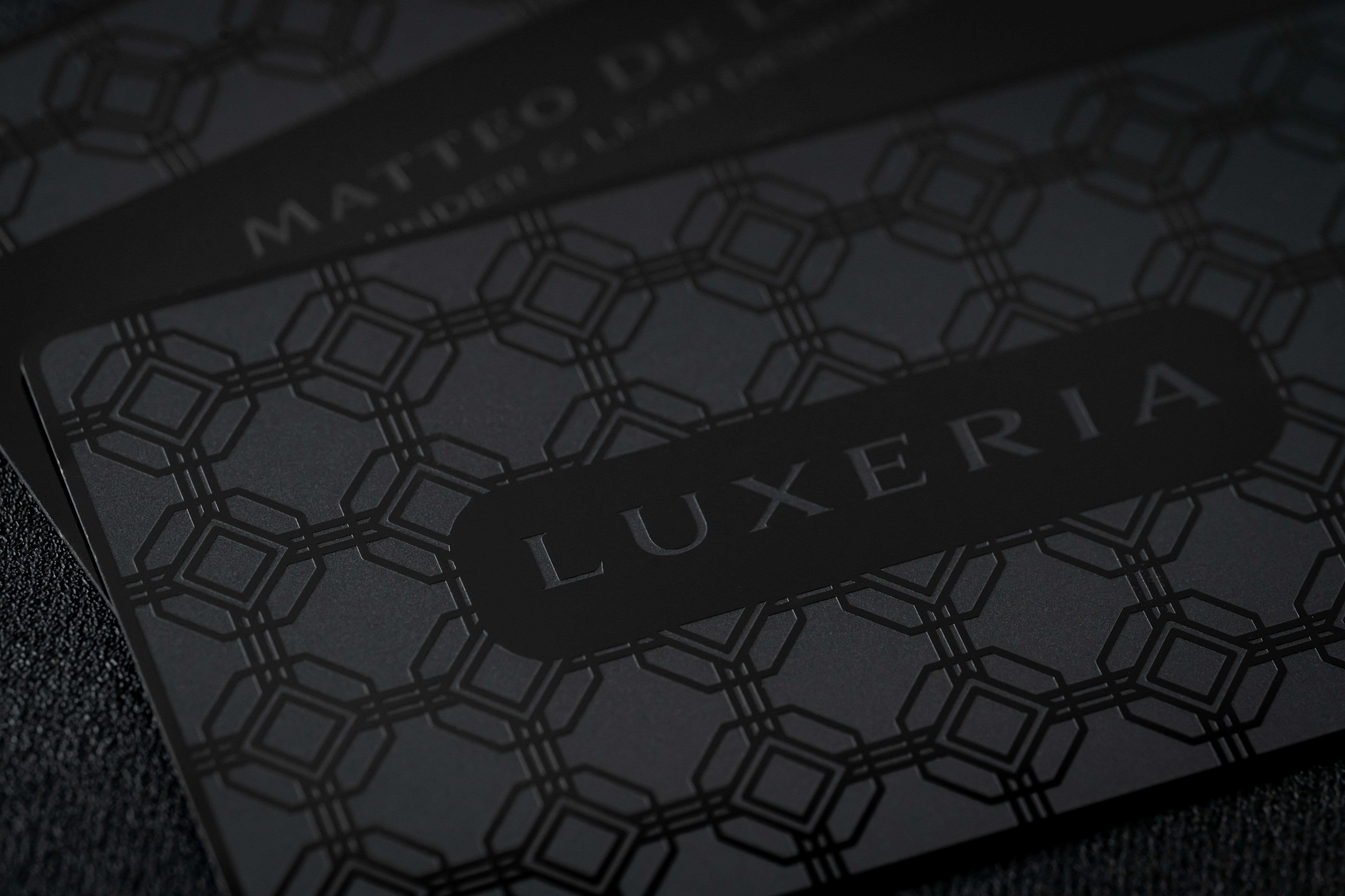 Close-up of Luxeria premium black metal business card featuring engraved geometric pattern and matte black finish