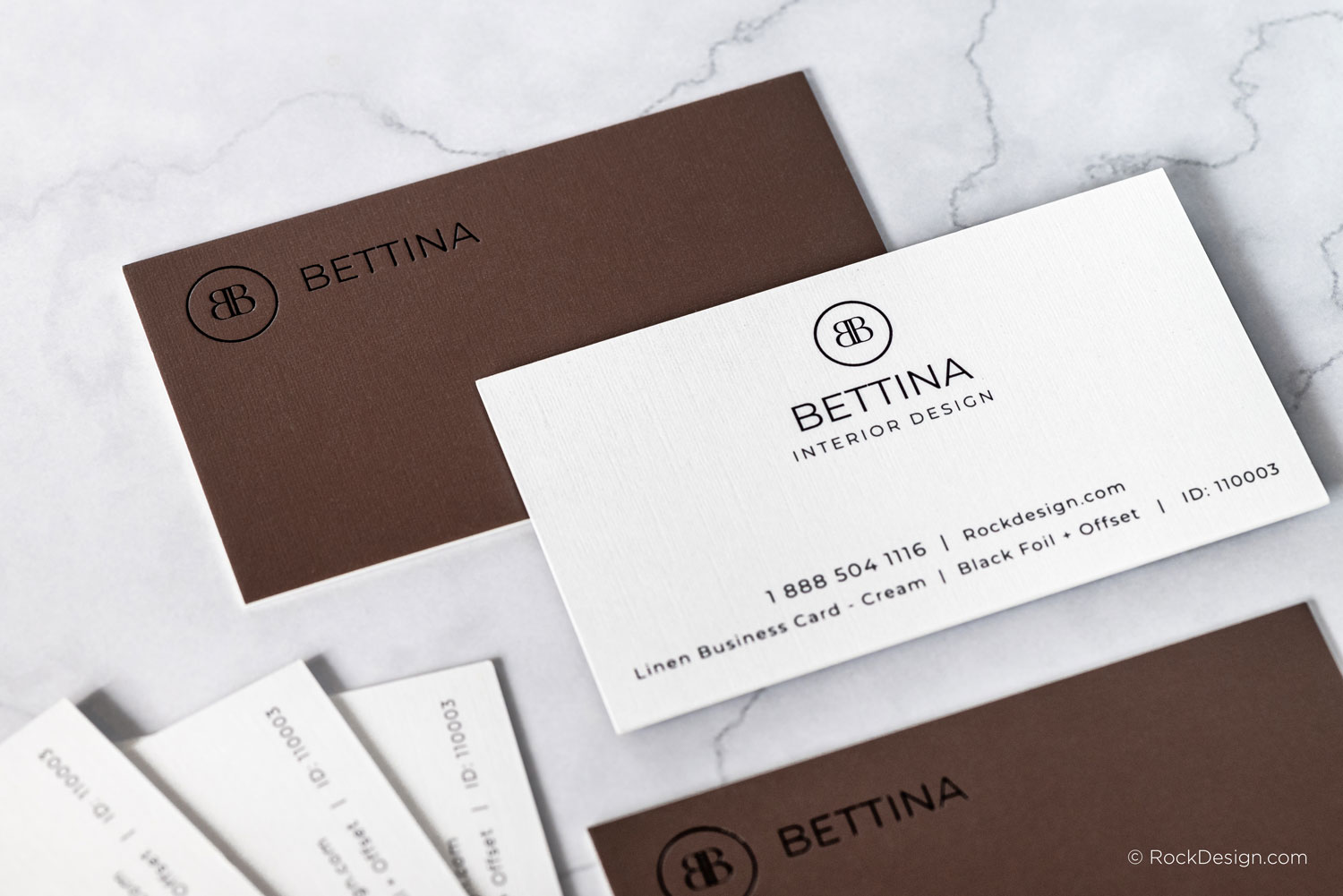 Linen cream business card with black foil for Bettina Interior Design, paired with a brown reverse side, displayed on a marble surface.